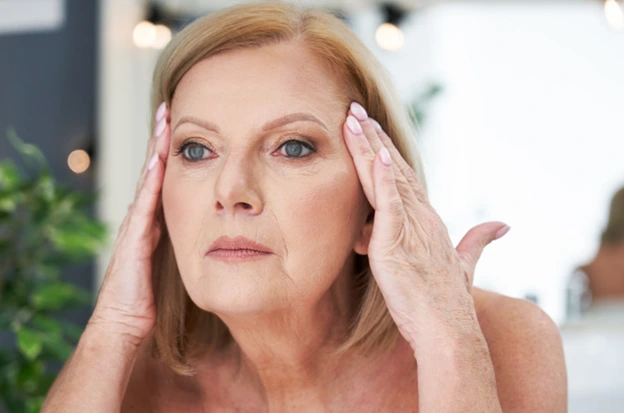 Mature woman examining her facial skin in the mirror.