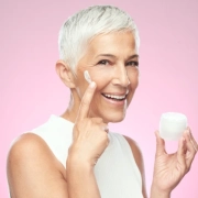 Senior woman applying anti-aging cream from a jar.