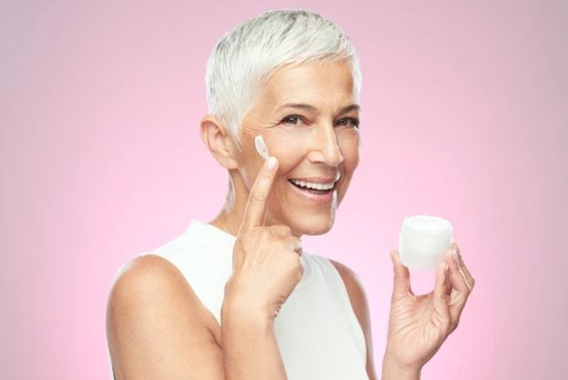 Senior woman applying anti-aging cream from a jar.