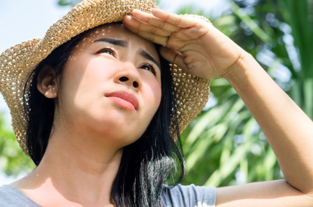 Woman in straw hat shielding her eyes from the sun.