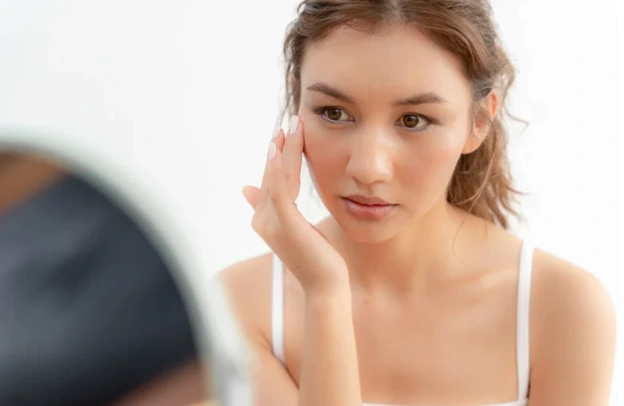 Young woman examining her face in a mirror.