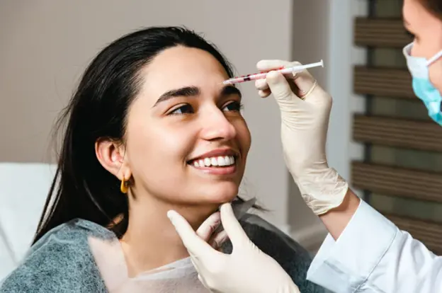 A smiling woman receiving a Botox treatment from a professional injector wearing gloves.