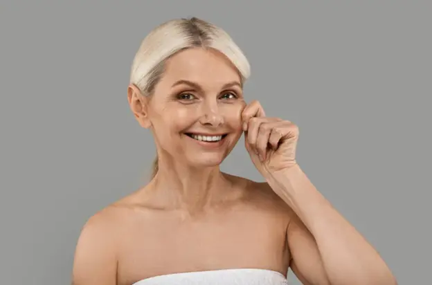 A smiling mature woman with healthy, firm skin gently pinching her cheek, showcasing the benefits of non-surgical skin tightening treatments.