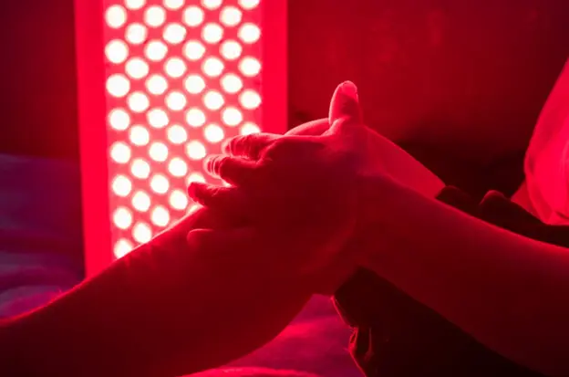 Hands receiving red light therapy from a professional LED light panel.